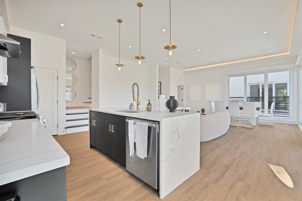 Kitchen with a large island, sink, stainless steel appliances, light stone countertops, and decorative light fixtures