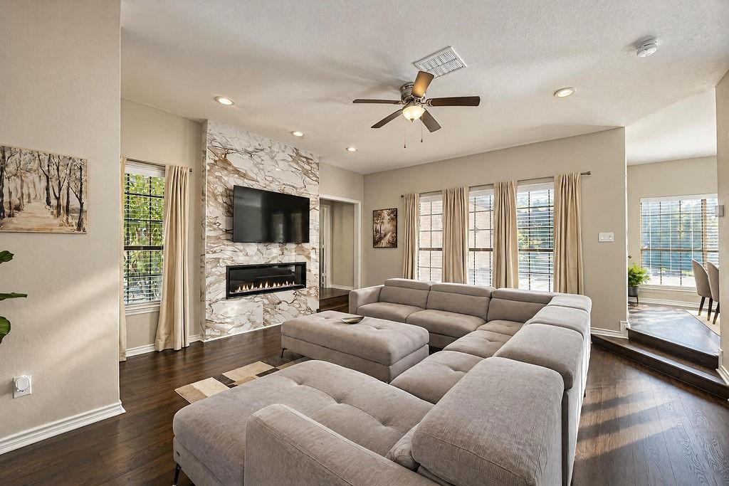 Living area featuring wood-finish flooring, a floor-to-ceiling stone-surround fireplace with an integrated linear electric insert, recessed lighting, and a ceiling fan