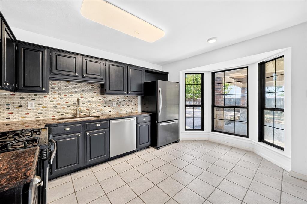 Kitchen featuring dark-finish shaker cabinetry, stone countertops, a multi-tone mosaic tile backsplash, stainless steel appliances, and a bay window