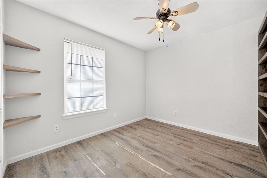 Wood-finish flooring, multi-pane window, built-in wooden corner shelving, floor-to-ceiling built-in wooden bookcase, and ceiling fan with integrated lighting