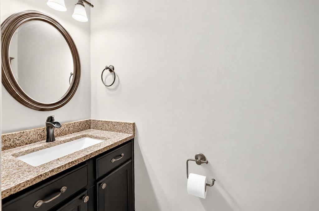 Bathroom vanity featuring dark-finished cabinetry, a stone-composite countertop, a drop-in rectangular sink, an oval wall-mounted mirror, and oil-rubbed bronze hardware