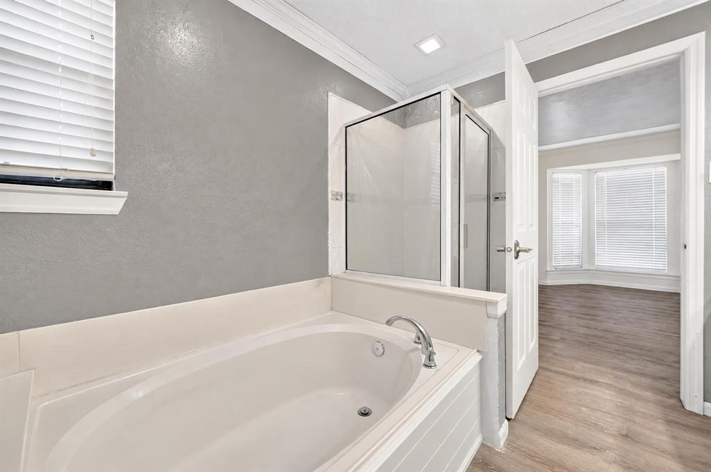 Soaking tub with chrome faucet, glass-enclosed shower, crown molding, and wood-finish flooring