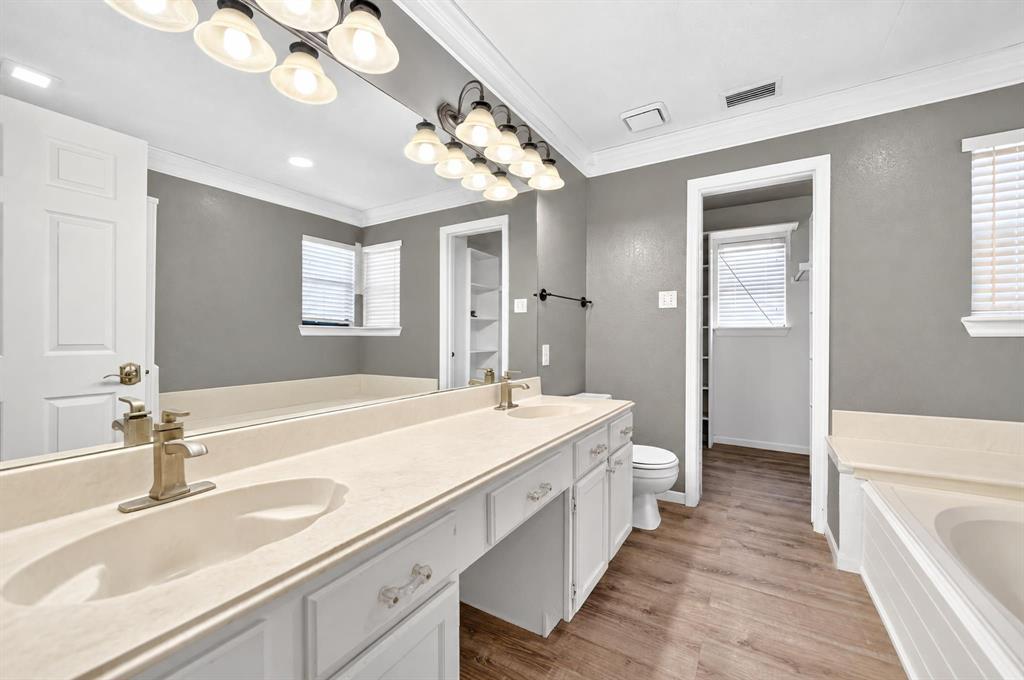 Dual-sink vanity with solid surface countertop, wood-finish flooring, full-width wall mirror, and integrated soaking tub