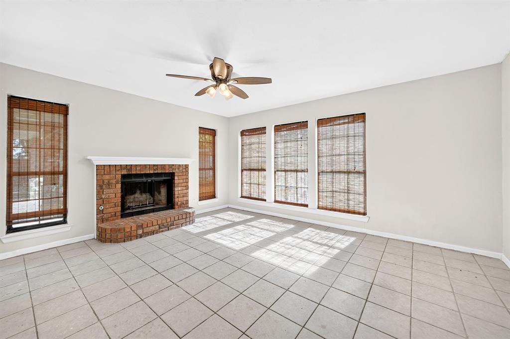 Brick fireplace with a raised hearth, large-format tile flooring, and a ceiling fan with integrated lighting