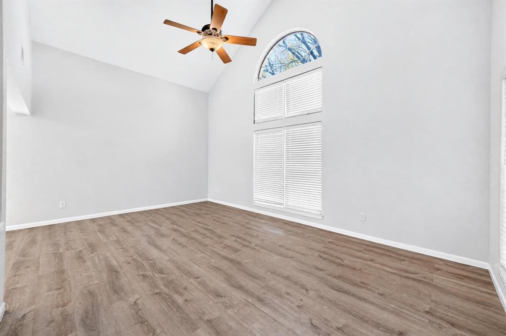 Vaulted ceiling featuring an arched window, wood-finish flooring, and a ceiling fan with integrated lighting