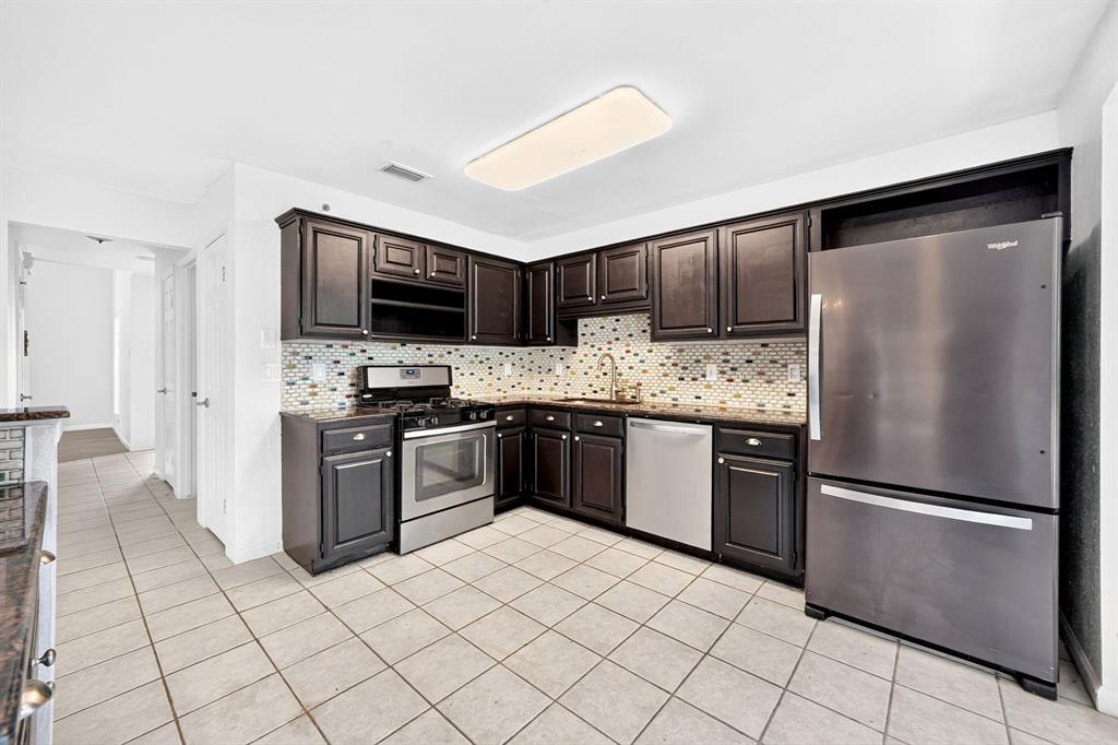 Kitchen featuring dark-finish cabinetry, stone-surface countertops, mosaic tile backsplash, stainless steel appliances, and tile flooring