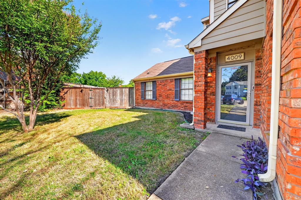 Exterior featuring red brick masonry, a covered entryway, paved concrete walkway, and wood privacy fencing