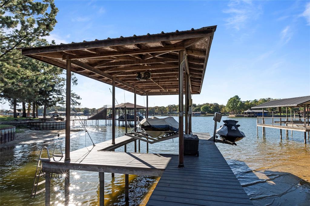 Covered boat dock featuring wood decking, a metal roof structure, and a ladder for water access