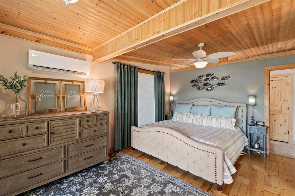 Wood-paneled ceiling with exposed beam, wood-finish flooring, wall-mounted ductless air conditioning unit, and solid wood interior door