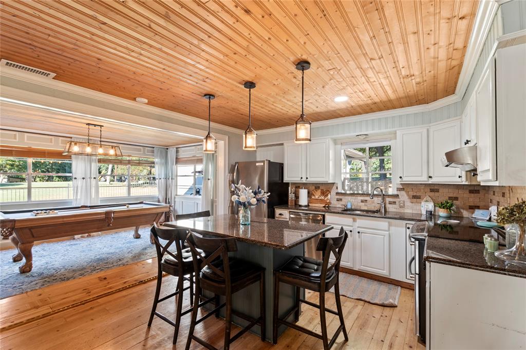 Kitchen featuring wood-plank ceiling, natural wood-finish flooring, white cabinetry, dark stone countertops, and three pendant lights over a central island Kitchen featuring wood-plank ceiling, natural wood-finish flooring, white cabinetry, dark stone countertops, and three pendant lights over a central island