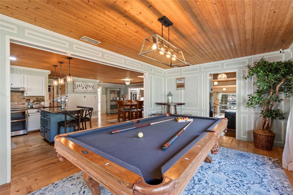 Tongue-and-groove wood plank ceiling, paneled wall detailing, natural wood-finish flooring, and a rectangular multi-light pendant fixture with a metal cage frame Tongue-and-groove wood plank ceiling, paneled wall detailing, natural wood-finish flooring, and a rectangular multi-light pendant fixture with a metal cage frame