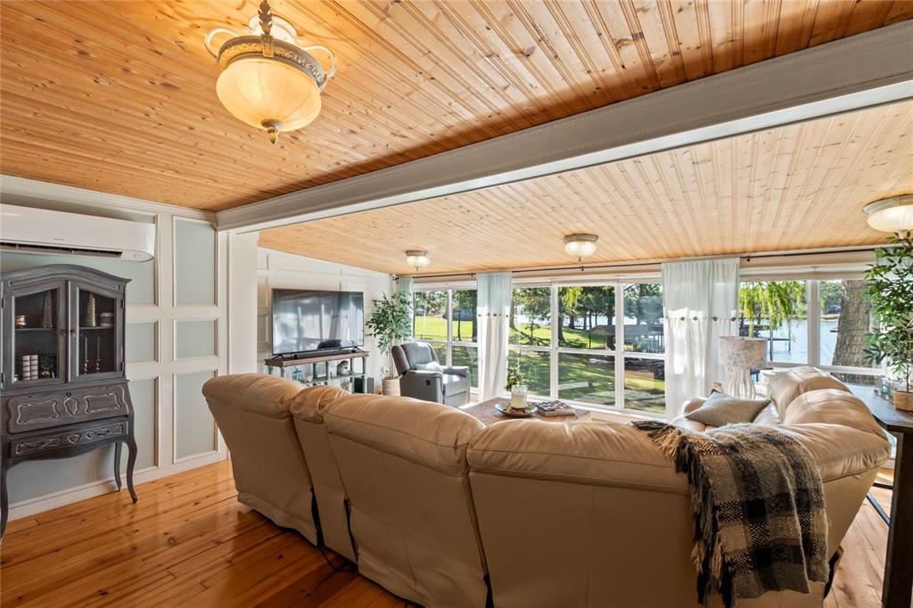 Vaulted natural wood-plank ceiling featuring decorative pendant lighting, wall-mounted ductless climate control system, paneled wainscoting, and expansive floor-to-ceiling windows