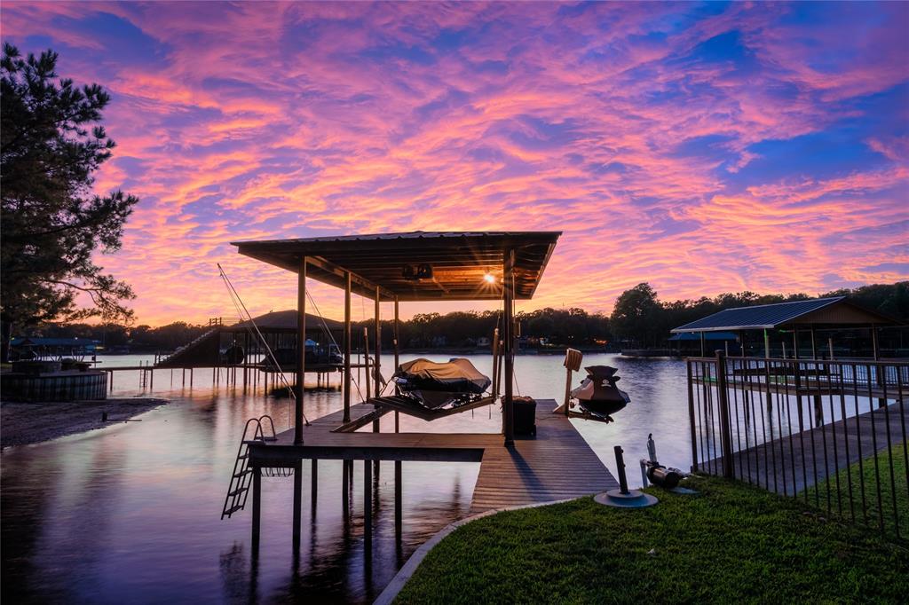 Waterfront property featuring a private covered boat dock, fixed pilings, metal roof structure, and metal perimeter fencing
