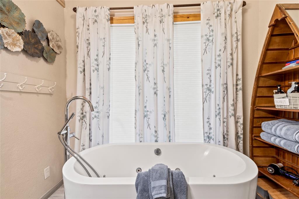 Freestanding jetted soaking tub featuring a chrome floor-mounted faucet and built-in wall-mounted coat rack