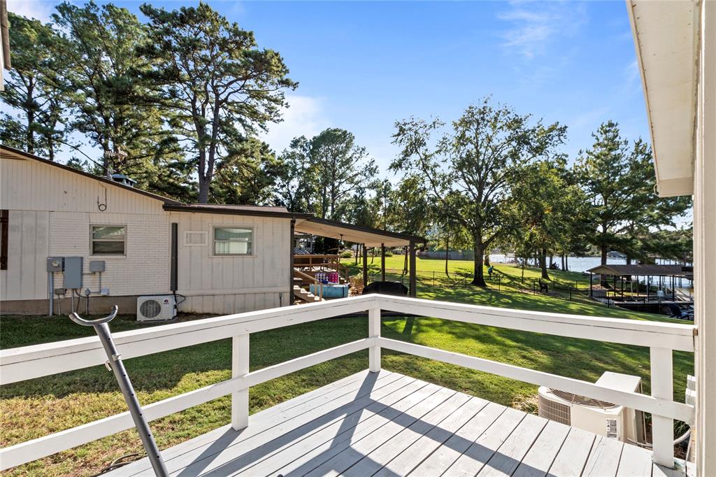 Elevated deck with white horizontal railing overlooking a grass lawn, mature trees, and waterfront access with a private pier