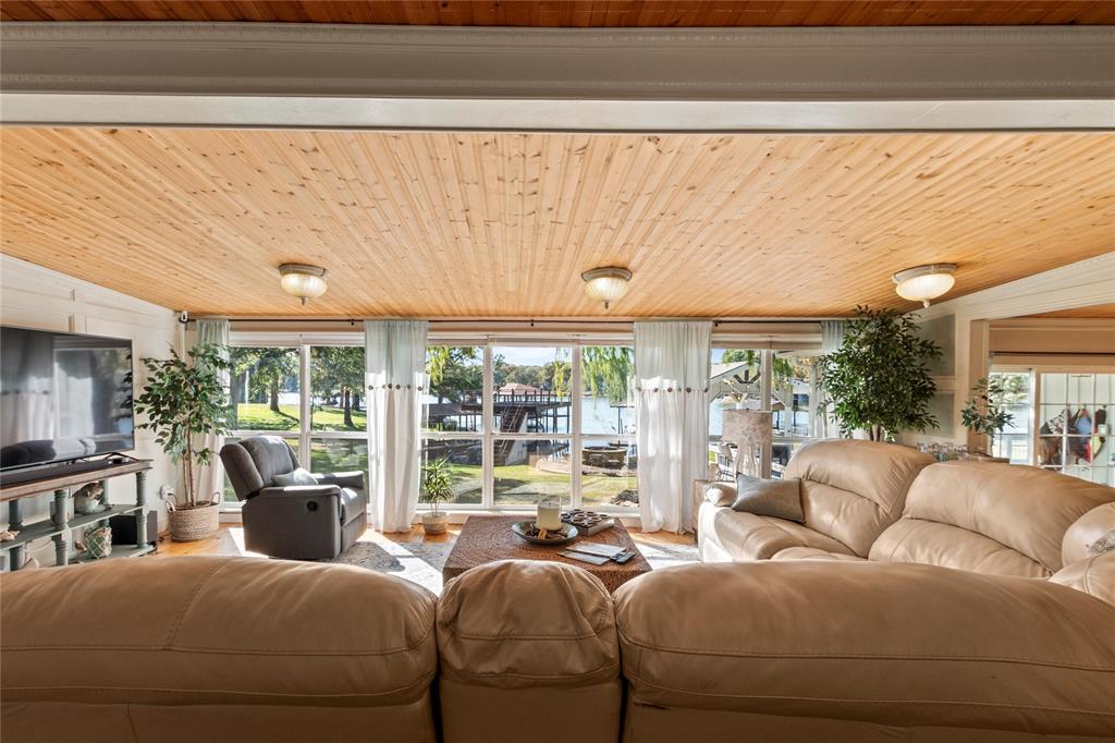 Natural wood-plank ceiling featuring flush-mount light fixtures, expansive floor-to-ceiling windows, and white vertical wainscoting