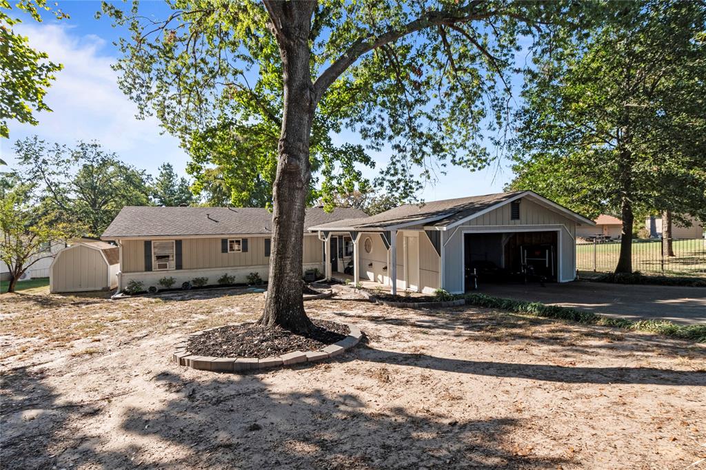 Single-story exterior featuring vertical siding, attached carport, detached storage shed, and stone tree surround
