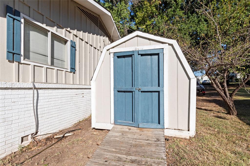 Exterior featuring a gambrel-roof storage shed with double doors, wood-sided home exterior with painted brick accents, and blue shutter detailing