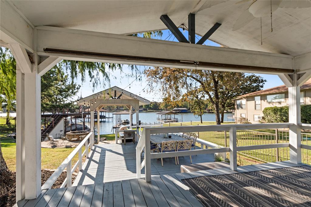 Covered outdoor patio featuring a vaulted ceiling, ceiling fan, and painted wood decking, leading to a wooden dock structure on the water
