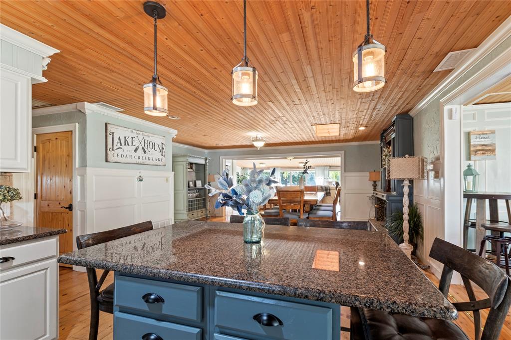 Kitchen featuring a central island with stone countertop, wood-plank ceiling, three industrial-style pendant lights, and beadboard wall paneling Kitchen featuring a central island with stone countertop, wood-plank ceiling, three industrial-style pendant lights, and beadboard wall paneling