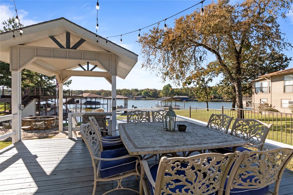 Covered outdoor deck featuring a gabled pavilion, overhead string lighting, metal railing, and direct water access