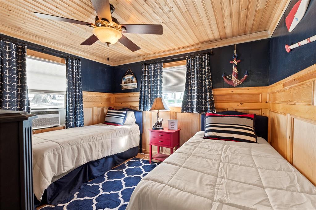 Room featuring natural wood plank ceiling, wood panel wainscoting, and a multi-blade ceiling fan