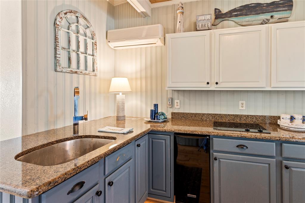 Kitchen area featuring two-tone cabinetry, stone-finish countertops, stainless steel undermount sink with a gooseneck faucet, vertical paneled wall treatments, and an integrated wall-mounted ductless climate control unit