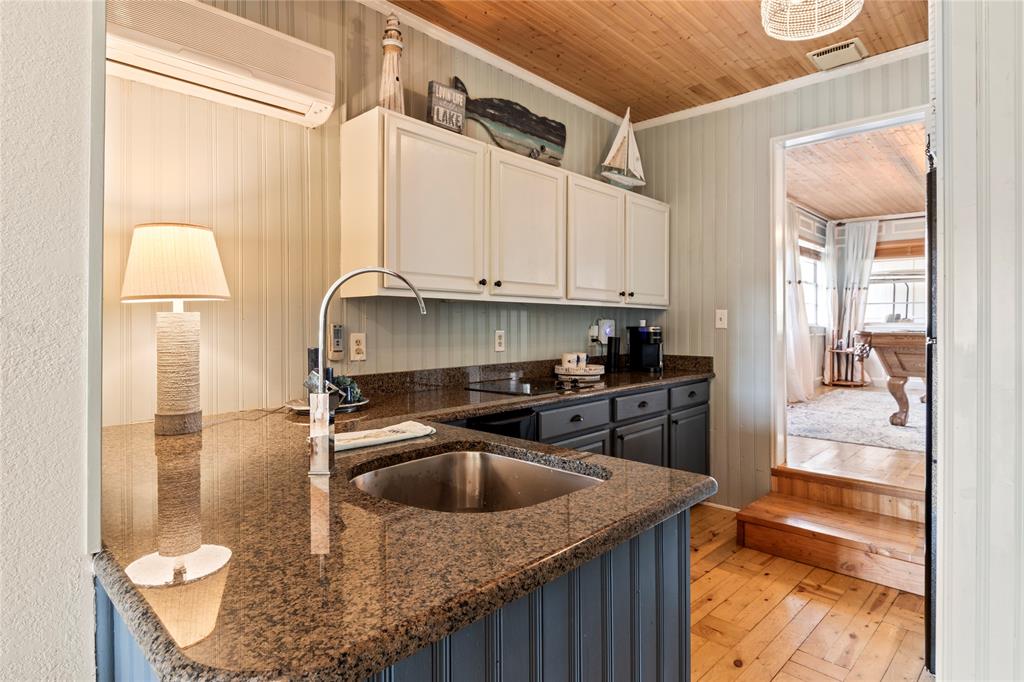 Kitchen featuring stone countertops, stainless steel undermount sink, dual-toned cabinetry, wood-finish flooring, and natural wood-plank ceiling