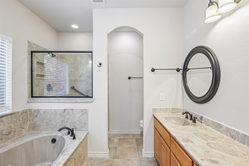 Soaking tub with stone-look surround, walk-in shower with glass enclosure, single vanity with stone-look countertop, integrated sink, and bronze-finish fixtures