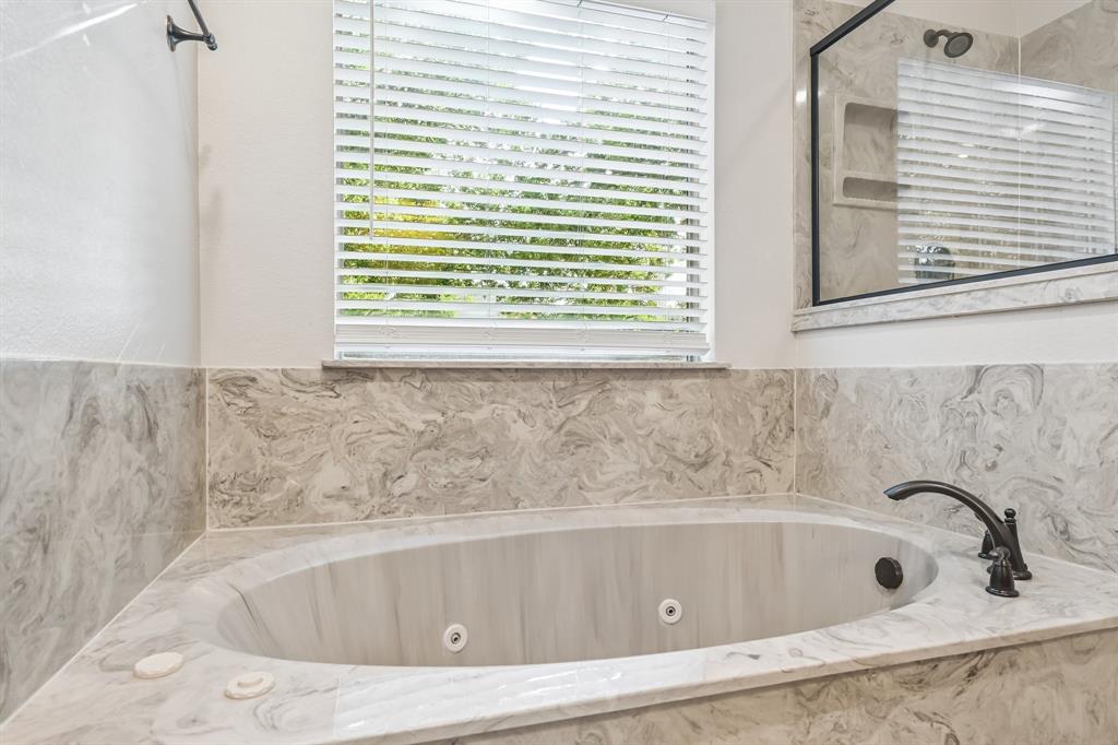 Soaking tub with a dark bronze faucet, surrounded by light-toned marble-look tile