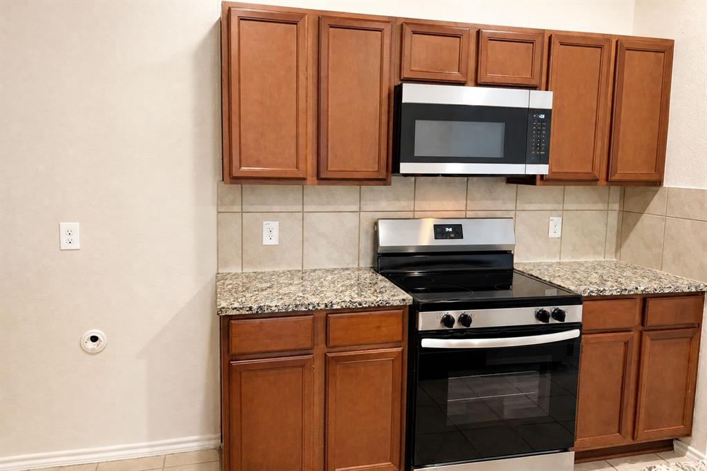 Kitchen featuring stained wood cabinetry, stone-finish countertops, ceramic tile backsplash, and stainless steel appliances including a built-in microwave and range