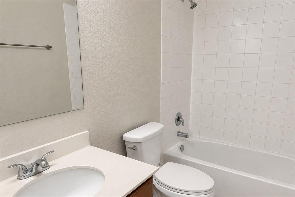 Bathroom featuring a vanity with an integrated sink and neutral countertop, wall-mounted mirror, white toilet, and a tub-shower combination with white tile surround