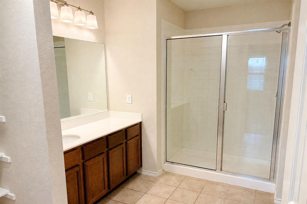 Bathroom featuring a vanity with wood-finish cabinetry, solid-surface countertop, full-width mirror, four-light fixture, and a glass-enclosed shower with tiled surround
