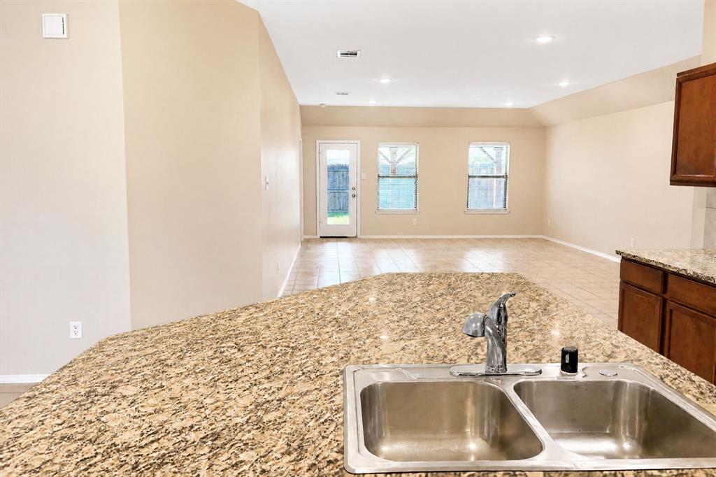 Stone-surface island countertop with a double-basin stainless steel sink, chrome faucet, ceramic tile flooring, recessed lighting, and wooden cabinetry