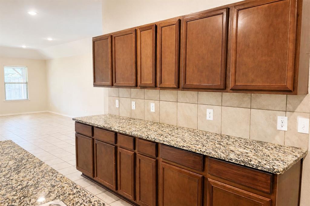 Kitchen area featuring medium-tone wood cabinetry, stone-surface countertops, and a ceramic tile backsplash