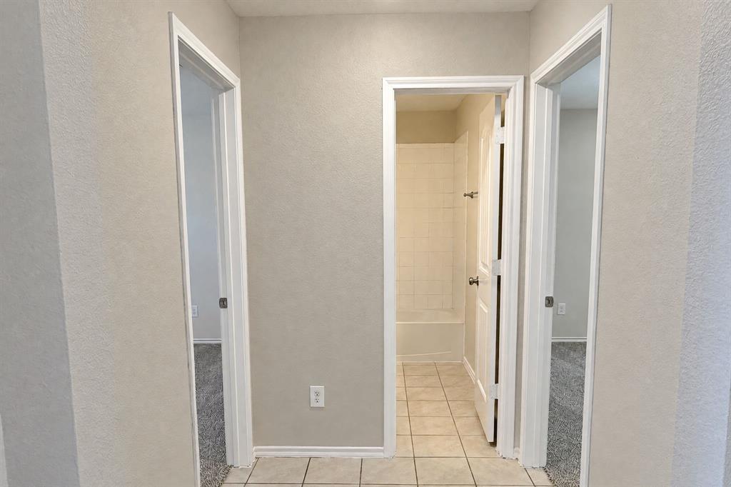 Neutral-toned interior hallway featuring tile flooring, three solid-core doors, and a tiled shower enclosure Neutral-toned interior hallway featuring tile flooring, three solid-core doors, and a tiled shower enclosure