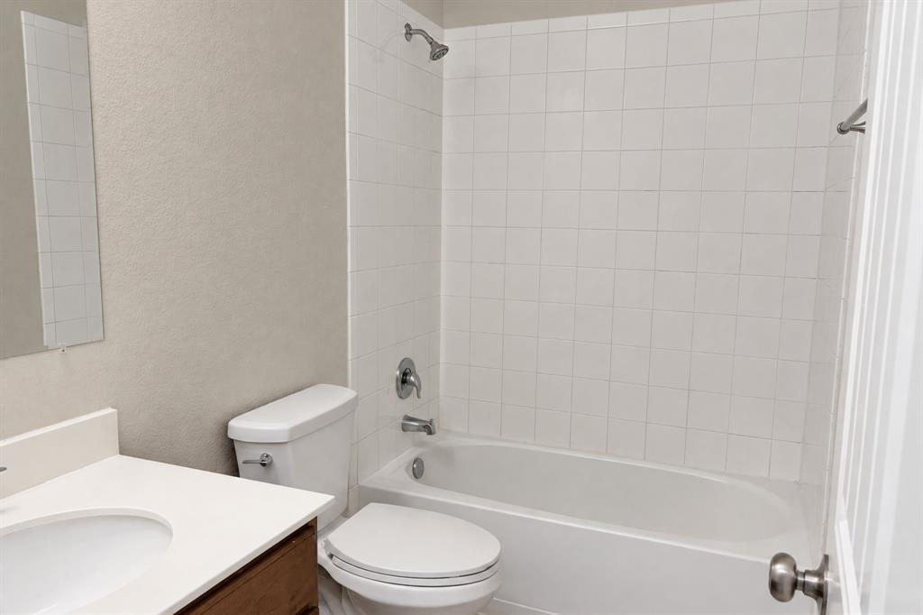 Bathroom featuring a vanity with a white countertop and integrated sink, a full-height white tile tub surround, a chrome shower fixture, and a standard bathtub Bathroom featuring a vanity with a white countertop and integrated sink, a full-height white tile tub surround, a chrome shower fixture, and a standard bathtub