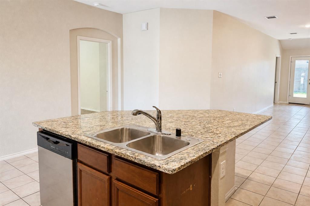 Kitchen island featuring stone-patterned countertops, a dual-basin stainless steel sink, a gooseneck faucet, built-in stainless steel dishwasher, and stained wood cabinetry