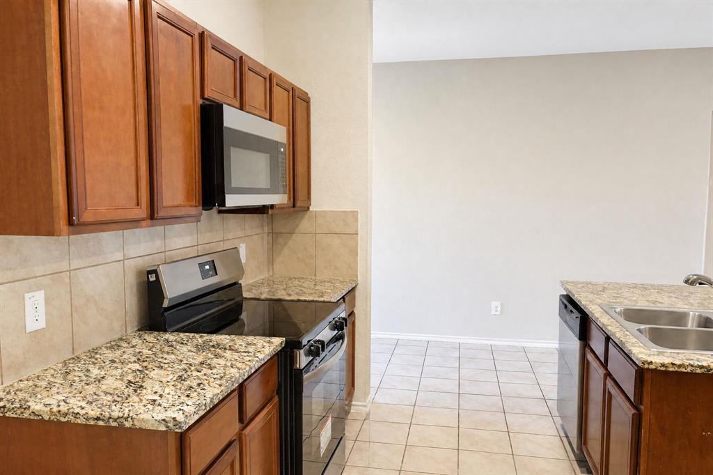 Kitchen featuring stained wood cabinetry, stone-surface countertops, ceramic tile backsplash, built-in microwave, and stainless steel double-basin sink