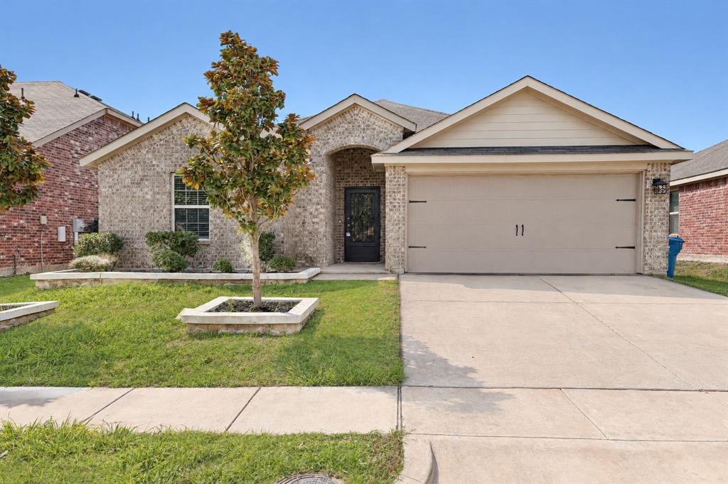 Single-story brick exterior featuring a recessed entryway, attached two-car garage, concrete driveway, and stone-bordered landscaping beds Single-story brick exterior featuring a recessed entryway, attached two-car garage, concrete driveway, and stone-bordered landscaping beds