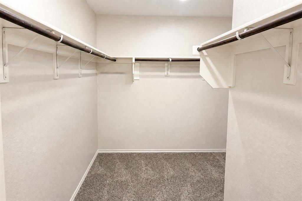 Walk-in closet featuring neutral carpeting, white wall finishes, and wrap-around built-in shelving with integrated hanging rods