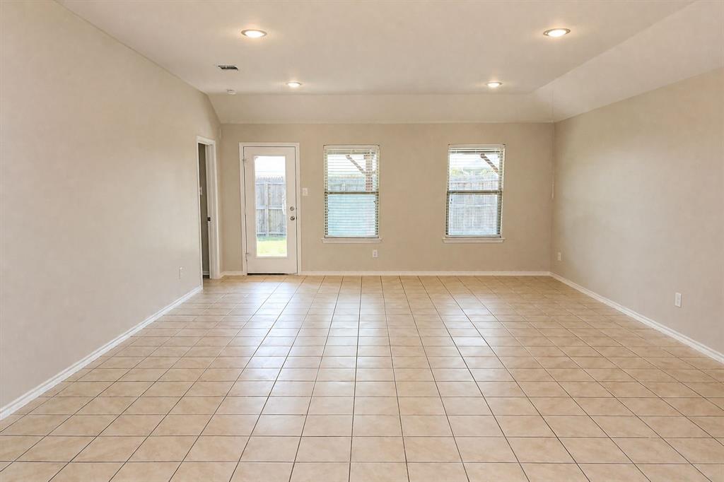 Neutral-toned interior featuring ceramic tile flooring, recessed lighting, and a vaulted ceiling with two windows and an exterior access door