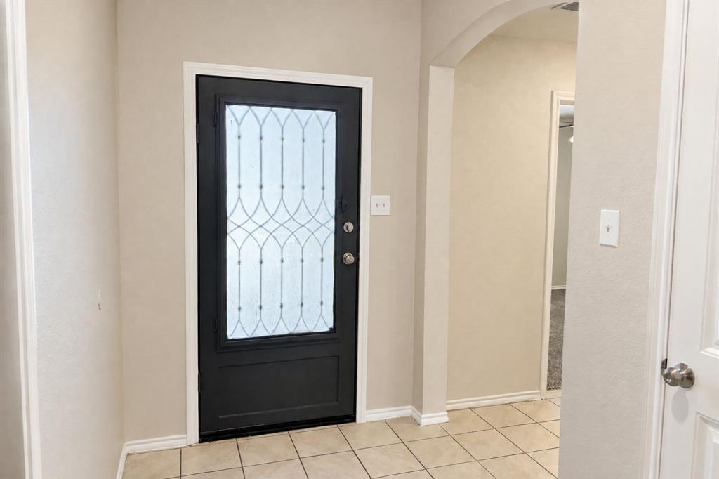 Entryway featuring a dark-toned front door with decorative glass inlay, neutral wall paint, arched architectural detail, and ceramic tile flooring Entryway featuring a dark-toned front door with decorative glass inlay, neutral wall paint, arched architectural detail, and ceramic tile flooring