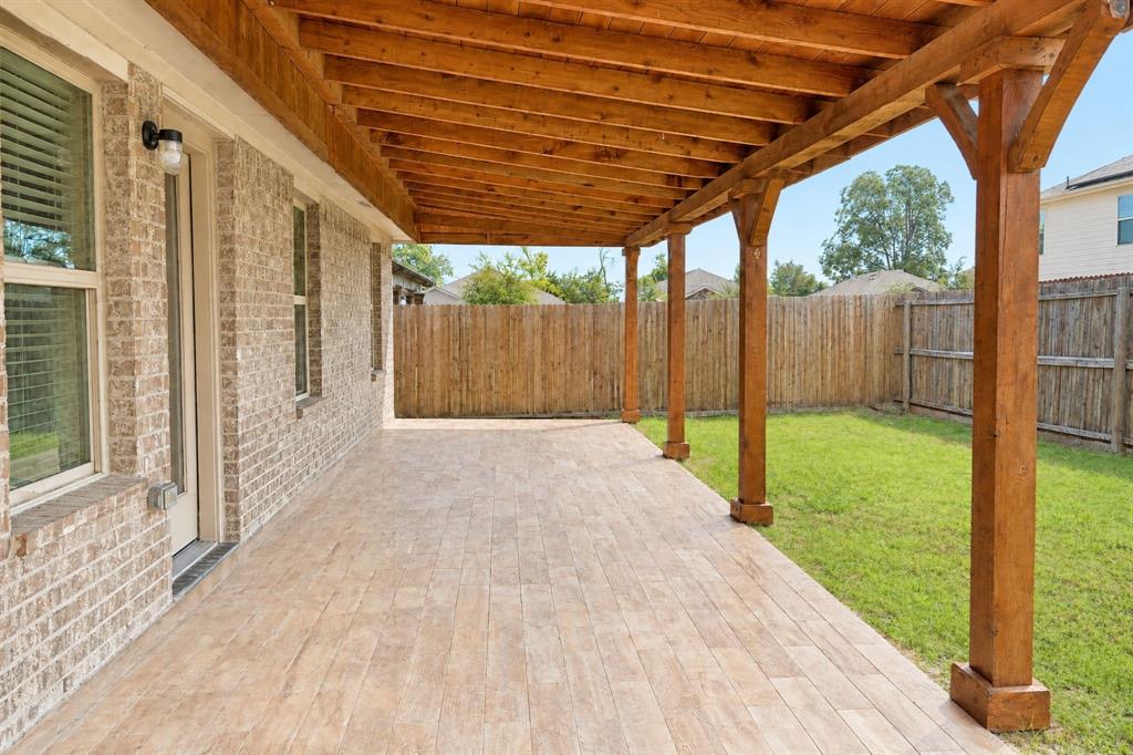 Covered patio with a wood-beam pergola, wood-finish tile flooring, brick exterior wall, and wooden privacy fencing