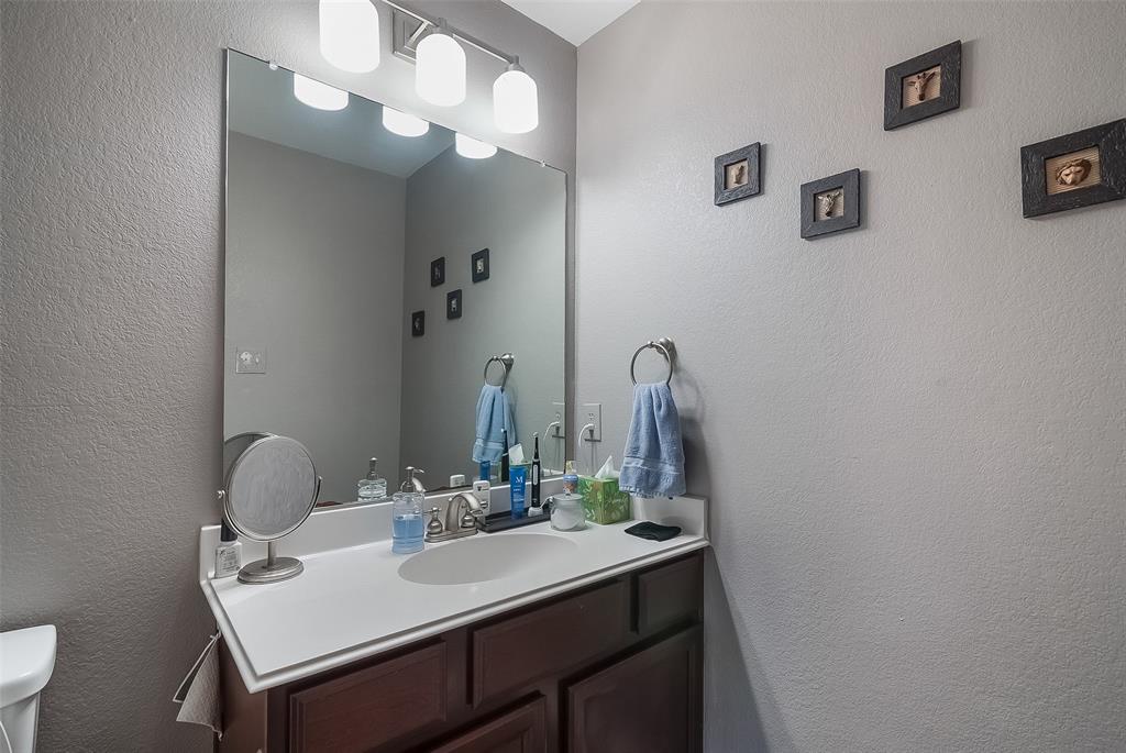 Bathroom vanity featuring a solid surface countertop, integrated sink basin, dark wood-finish cabinetry, a full-width wall mirror, and a four-light fixture