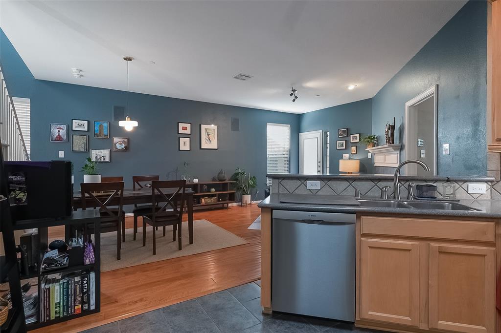 Kitchen featuring wood-finish cabinetry, a stainless steel dishwasher, a dual-basin sink, and tile backsplash, complemented by wood-finish flooring throughout the main area