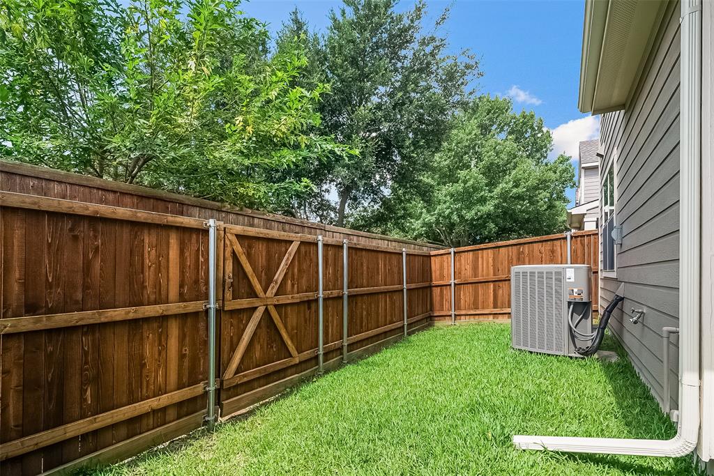 Side yard featuring a stained wood privacy fence with metal support posts, grass lawn, and exterior HVAC unit