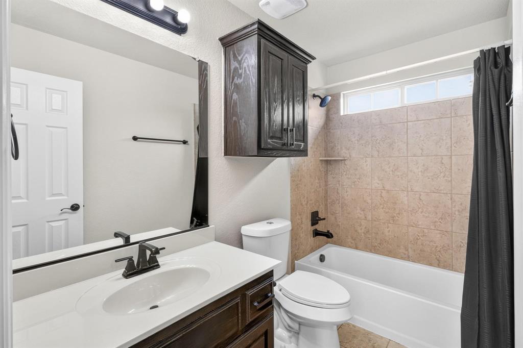 Vanity with a solid-surface countertop and integrated oval sink, dark wood-finish cabinetry, wall-mounted storage cabinet, matte black hardware, and a tub-shower combination with tiled surround