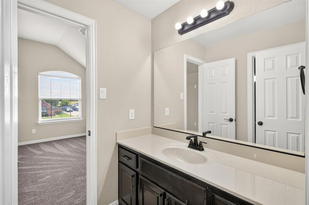 Vanity featuring a solid-surface countertop, integrated oval sink, matte black faucet, dark wood-finish cabinetry, and a full-width mirror with a four-light fixture