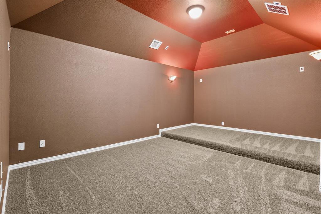Interior space featuring a raised tiered floor, vaulted ceiling, neutral wall-to-wall carpeting, wall-mounted sconce lighting, and flush-mount overhead lighting